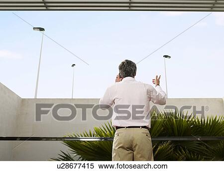 Man standing on balcony using mobile phone, rear view View Large Photo Image Stock Photography - Man standing on balcony using mobile phone, rear view. Fotosearch