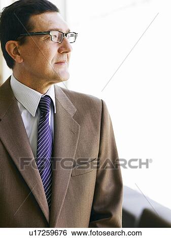 Stock Photograph - Mature businessman standing by window. Fotosearch
