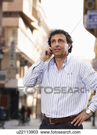 Stock Image - Mature man standing in street using mobile phone. Fotosearch