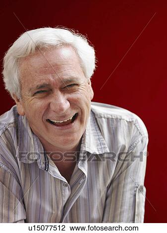 Stock Image - Senior man standing beside red wall, laughing, portrait. Fotosearch