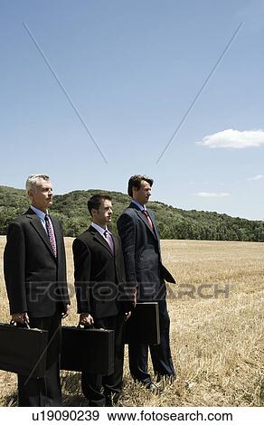 Three businessmen standing in a row in field. View Large Photo Image Stock Photo - Three businessmen standing in a row in field.. Fotosearch