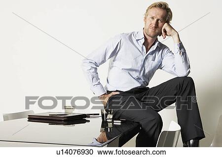 Stock Image - Young businessman seated on desk.. Fotosearch