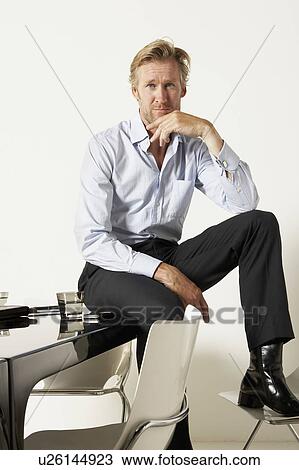 Young businessman seated on desk. View Large Photo Image Stock Image - Young businessman seated on desk.. Fotosearch