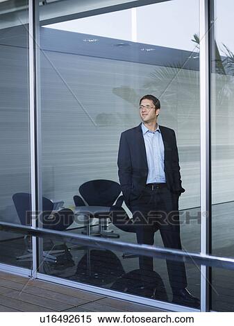 Young businessman standing at window in office View Large Photo Image Stock Photography - Young businessman standing at window in office. Fotosearch