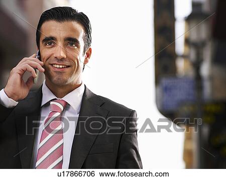 Stock Photograph - Young businessman using mobile phone in street, smiling. Fotosearch