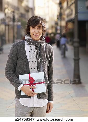 Young man standing in street holding gift, smiling, portrait View Large Photo Image Stock Photo - Young man standing in street holding gift, smiling, portrait. Fotosearch