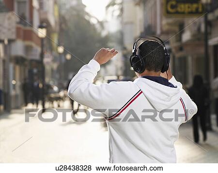 Young man standing in street wearing headphones, rear view View Large Photo Image Stock Photo - Young man standing in street wearing headphones, rear view. Fotosearch
