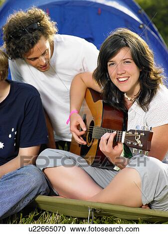 Stock Image - Girl playing guitar while male looks over. Fotosearch