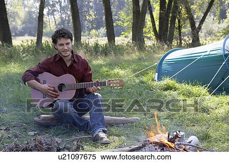 Stock Photography - Man at campsite playing guitar and smiling.. Fotosearch