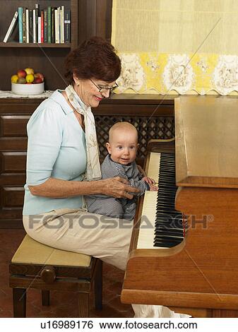 Stock Photograph - Senior grandmother playing piano with baby grandson (1-3 months). Fotosearch