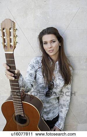 Stock Image - Woman standing and holding up a guitar.. Fotosearch