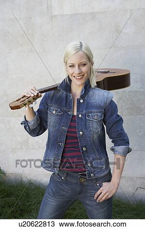 Stock Image - Woman standing holding a guitar smiling.. Fotosearch