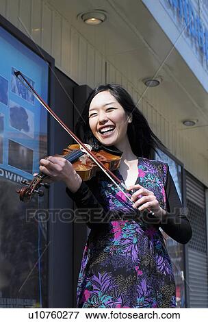 Young female busker playing violin outside cinema, smiling View Large Photo Image Stock Photo - Young female busker playing violin outside cinema, smiling. Fotosearch