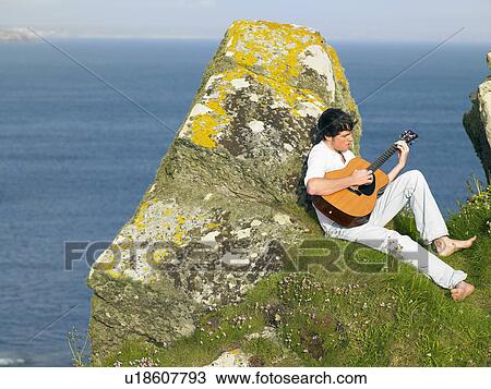 Young man sitting by a cliff playing the guitar. View Large Photo Image Stock Image - Young man sitting by a cliff playing the guitar.. Fotosearch