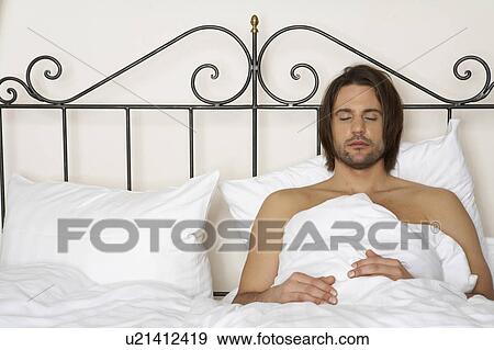 Stock Photo - young man lying in bed, eyes closed. Fotosearch