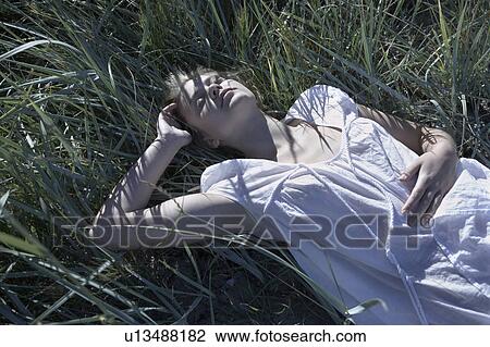 Stock Image - Young woman lying in long grass.. Fotosearch