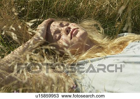 Stock Image - Young woman lying in long grass.. Fotosearch