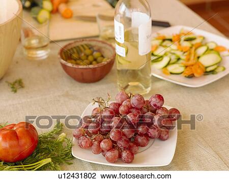 Stock Image - Black grapes, white wine, olives and salad on dining table (still life). Fotosearch