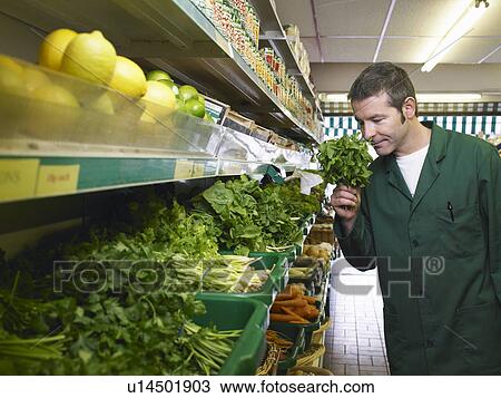 Stock Image - Grocer smelling herbs. Fotosearch