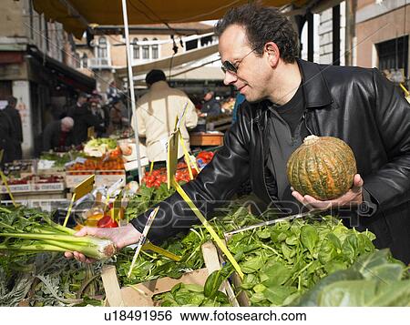Stock Photograph - Man choosing vegetables at Rialto market. Venice, Italy.. Fotosearch