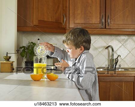 Stock Image - Young boy making orange juice in kitchen.. Fotosearch