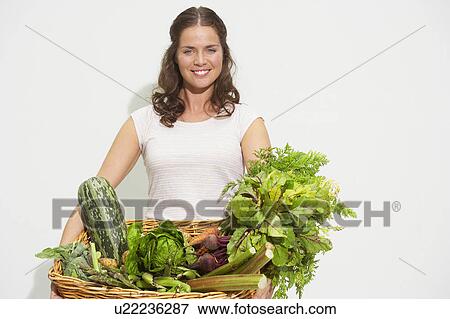 Stock Photo - Young woman with large basket of organic vegetables.. Fotosearch