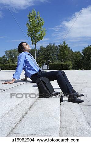 Businessman sitting on steps with laptop sunbathing smiling park in background. View Large Photo Image Picture - Businessman sitting on steps with laptop sunbathing smiling park in background.. Fotosearch