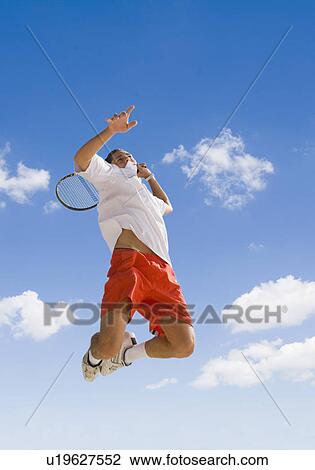 Stock Image - Man playing tennis against blue sky.. Fotosearch