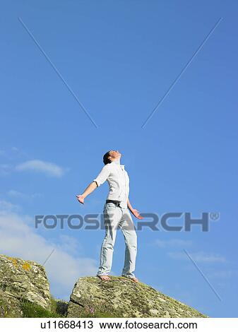 Young man standing on cliff with head towards the sky. View Large Photo Image Stock Image - Young man standing on cliff with head towards the sky.. Fotosearch