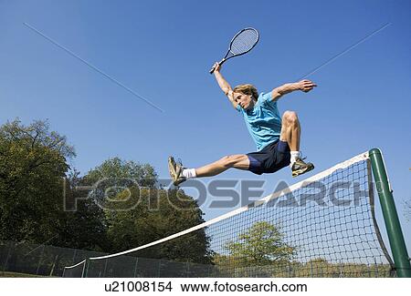 Picture - Young man with tennis racket jumping net.. Fotosearch
