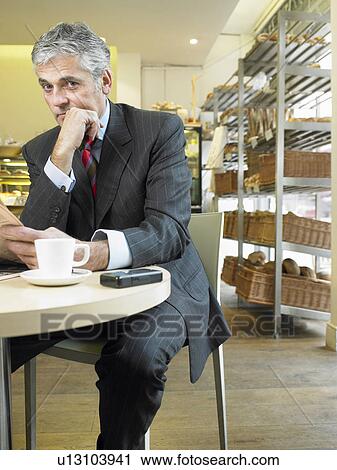 Stock Image - Mature businessman sitting in cafe reading newspaper, portrait. Fotosearch