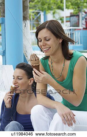 Two smiling women sitting on steps while eating ice cream. View Large Photo Image Stock Photograph - Two smiling women sitting on steps while eating ice cream.. Fotosearch