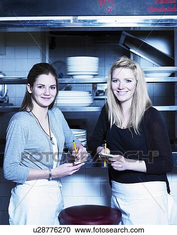 Two young waitresses holding notepads, smiling, portrait View Large Photo Image Stock Image - Two young waitresses holding notepads, smiling, portrait. Fotosearch