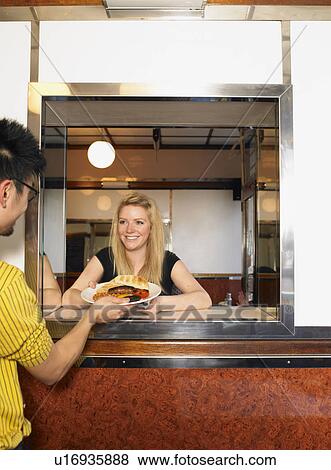Stock Photo - Waitress serving plate of fried food to man in cafe, smiling. Fotosearch