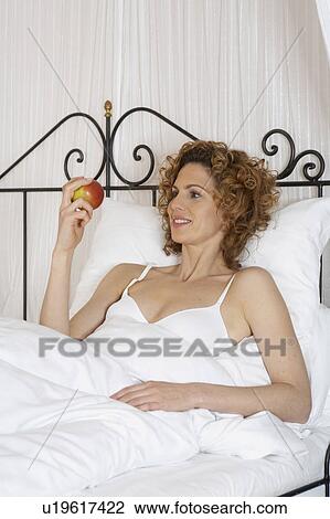 Stock Image - woman in bed holding apple. Fotosearch