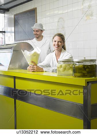 Stock Image - Woman serving in fish and chip shop, male colleague in background. Fotosearch