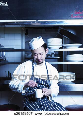 Young chef taking break in kitchen holding cup, smiling View Large Photo Image Stock Photo - Young chef taking break in kitchen holding cup, smiling. Fotosearch