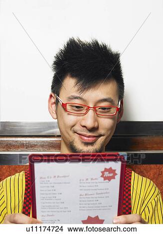 Picture - Young man looking at cafe menu, smiling, close-up. Fotosearch