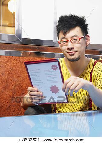 Young man looking at cafe menu, smiling, close-up View Large Photo Image Stock Image - Young man looking at cafe menu, smiling, close-up. Fotosearch