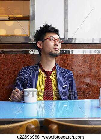 Young man sitting in cafe holding cup View Large Photo Image Stock Photo - Young man sitting in cafe holding cup. Fotosearch