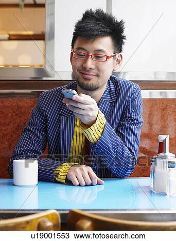 Stock Image - Young man sitting in cafe using mobile phone, smiling. Fotosearch