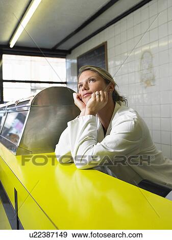 Stock Photo - Young woman resting elbows on counter in fish and chip shop. Fotosearch