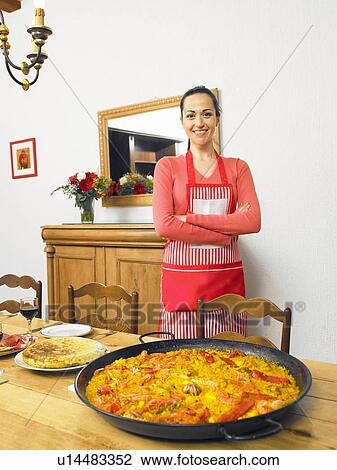 Young woman standing by large dish of paella on dining table, smiling, portrait View Large Photo Image Stock Image - Young woman standing by large dish of paella on dining table, smiling, portrait. Fotosearch