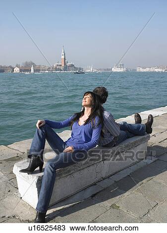 Couple sitting back to back on a stone bench near water. Venice, Italy. View Large Photo Image Stock Image - Couple sitting back to back on a stone bench near water. Venice, Italy.. Fotosearch