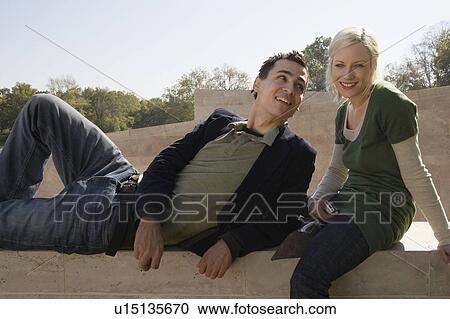 Couple sitting outdoors smiling with the woman holding a camera. View Large Photo Image Stock Image - Couple sitting outdoors smiling with the woman holding a camera.. Fotosearch