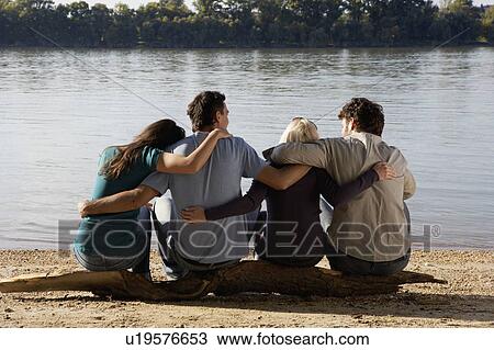 Four friends sitting on log by a lake with arms around each other. View Large Photo Image Stock Image - Four friends sitting on log by a lake with arms around each other.. Fotosearch