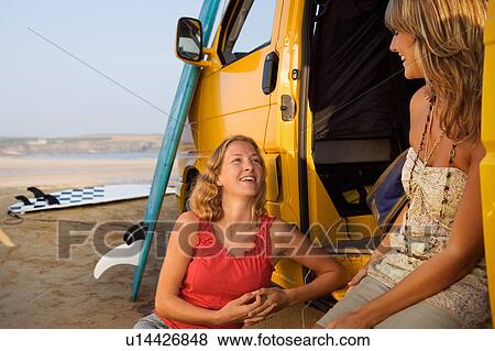 Two women sitting by a van smiling with surfboards in background. View Large Photo Image Stock Photo - Two women sitting by a van smiling with surfboards in background.. Fotosearch