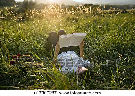 Stock Photo - Woman lying in grass reading.. Fotosearch