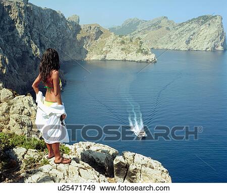 Stock Photo - Woman standing on a large rock with a speedboat going by.. Fotosearch