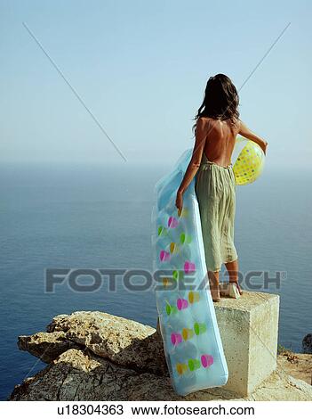 Woman standing on rock over looking the sea holding a beach ball and a lilo. View Large Photo Image Stock Image - Woman standing on rock over looking the sea holding a beach ball and a lilo.. Fotosearch